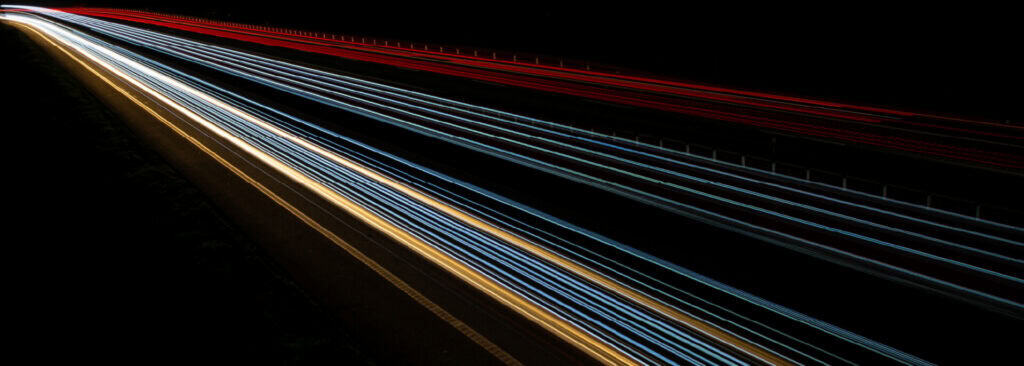 Long-exposure light trails from highway traffic streak diagonally across a dark nighttime landscape.