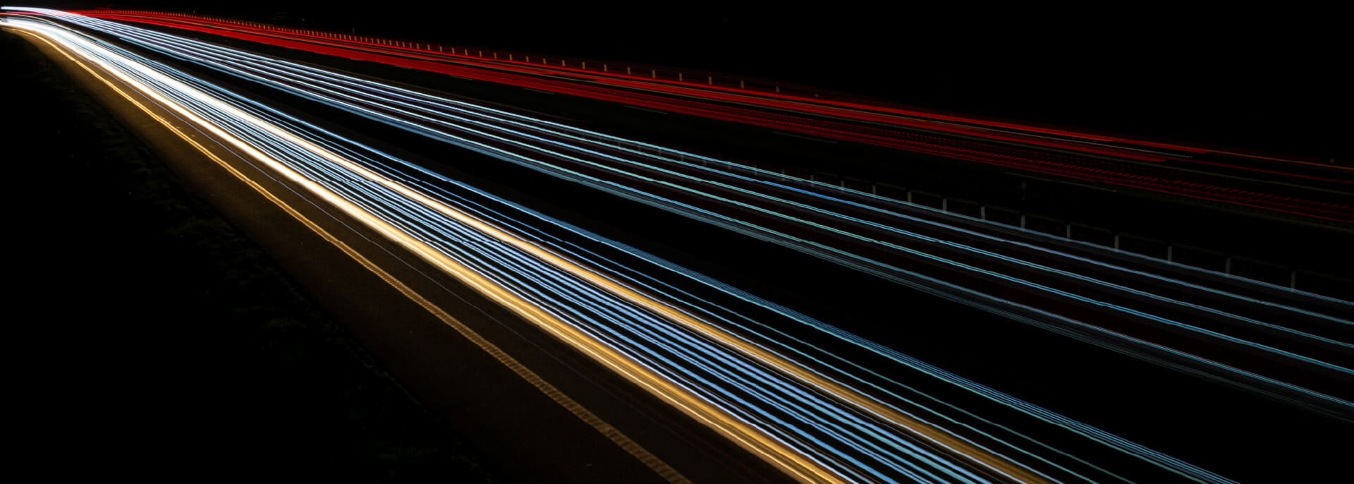 Long-exposure light trails from highway traffic streak diagonally across a dark nighttime landscape.